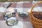 Picnic set, three persons. metal Cutlery, thermos, plates, tea cups. brown plaid and napkin from the lake in the background. green