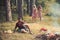 Picnic at sunny meadow. Two girls wandering in woods while thoughtful man is sitting on grass. Brutal bearded man