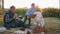 Picnic on sunset background, boy kisses grandparent sitting on plaid with basket near dog and hedgehog
