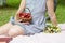 On a picnic  a woman sits on a plaid on the grass and holds a basket with red ripe strawberries and a bouquet of wild flowers.
