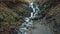 Pictorial foaming waterfall near grey ground path in autumn