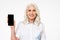 Picture of adult woman with grey hair smiling and doing commercial with presenting mobile phone, isolated over white background