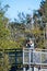 A picture of an Asian man taking a photo from atop a viewing tower in a park.