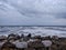 A picture of beach with rocks on the shore and cloudy sky on background. The sea is violent with strong waves in this picture.