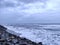 A picture of beach with rocks on the shore and cloudy sky on background. The sea is violent with strong waves in this picture.