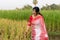A picture of a Bengali girl wearing a red and white sari in a vast paddy field in autumn