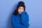 Picture of bored unsatisfied dark haired young female standing isolated over blue background in studio, touching her face with