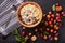 Picture of bowl of porridge in deep plate, spoon, blueberries, aliches and plums, caheckered kitchen towel on dark wooden