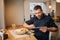 A picture of businessman sitting at table and working. He is using tablet. There is a plate with tasty food and drink on