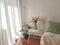 Picture captures a cozy bedroom, featuring two vibrant vases of flowers and a bright white chair