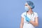 Picture of Caucasian doctor woman isolated over blue studio background, wearing hat, gloves and flumask, pointing aside with her