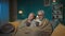 In the picture, an elderly couple is sitting on a sofa in a room under a blanket. They are holding a cup of hot tea or