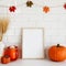 Picture frame mockup with orange pumpkins, vase of wheat, garland of leaves on wall tile background. Cozy home interior with