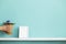 Picture frame mockup. White shelf against pastel turquoise wall with hand putting down potted violet