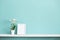Picture frame mockup. White shelf against pastel turquoise wall with potted orchid plant
