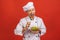 Picture of happy young senior chief cook in uniform standing isolated over red wall background, holding and eating salad