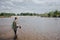 A picture of man standing in water and fishing. He is holding spinning in hands and looking at water. Guy has fishing