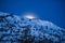 A picture of the moon peeking out from behind some mountains.