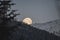 A picture of the moon peeking out from behind some mountains.