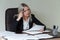 Picture of pensive businesswoman with big notepad in suit sitting at the table with documents.