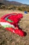 Picture of red and blue parachutes laying on dry ground with hills and trees on the background