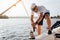 Picture of sailor stands on yacht and winds rope around. He is calm and concentrated. Young man works hard. He prepares