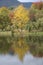 A picture of a stunning autumnal landascape with lots of colors, trees and a romantic lake surrounded by high mountains