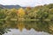 A picture of a stunning autumnal landascape with lots of colors, trees and a romantic lake surrounded by high mountains