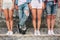 A picture of teens` legs. Three of them are standing straight while man in jeans is holding left leg over right one