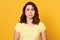 Picture of upset sad miserable young woman having frowned facial expression, standing isolated over yellow background in studio,