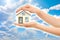 Picture of woman's hands holding a house against sky