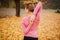 Picture of young woman stands in autumn park and look to left. She stretches hands. Woman keep them together behind back.