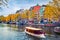Picturesque autumn cityscape of Amsterdam. Splendid view of famous Dutch channels and excursion boat. Colorful morning landscape i
