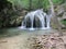 A picturesque mountain river at the bottom of the gorge forms a cascade of waterfalls against the background of boulders, green mo