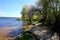 A picturesque narrow beach on the river bank. The branches of the willow are lowered to the water