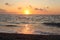 Picturesque orange sunset on a pebble beach, the sun`s rays are reflected in the sea waves and sea foam, the sea coast of Calabria