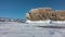 A picturesque rocky island rises above an icy lake against a blue sky.