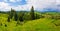 Picturesque spring idyllic scene of the Carpathians, green grass field in front of a wooden cottage surrounded by coniferous
