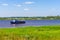 Picturesque summer landscape with blue sky, meadow, river and floating ship in sunny day. Beautiful natural background with vessel