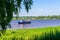 Picturesque summer landscape with blue sky, meadow, river and floating ship in sunny day. Beautiful natural background with vessel