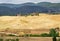 Picturesque Tuscany landscape with rolling hills, valleys, sunny fields, cypress trees, rural road, houses on a hill.