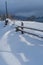 Picturesque waved shadows on snow from wood fence. Alpine mountain winter hamlet outskirts, snowy path, fir forest on far misty