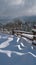 Picturesque waved shadows on snow from wood fence. Alpine mountain winter hamlet outskirts, snowy path, fir forest on far misty