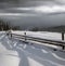 Picturesque waved shadows on snow from wood fence. Alpine mountain winter hamlet outskirts, snowy path, fir forest on far misty