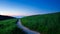 Picturesque winding path through a green grass field in hilly area at sunset