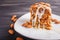 Pie with caramel, white milk sauce and almonds on a white plate on a black wooden background