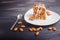 Pie with caramel, white milk sauce and almonds on a white plate on a black wooden background