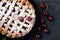 Pie with cherries, icing sugar, black plate and cherries