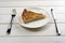 Pie on a white plate with cutlery lying on a white wooden table