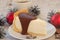 A a piece of an appetizing cheese cake with melted chocolate on it, a cup of coffee, silver cones, cinnamon sticks and Christmas-t